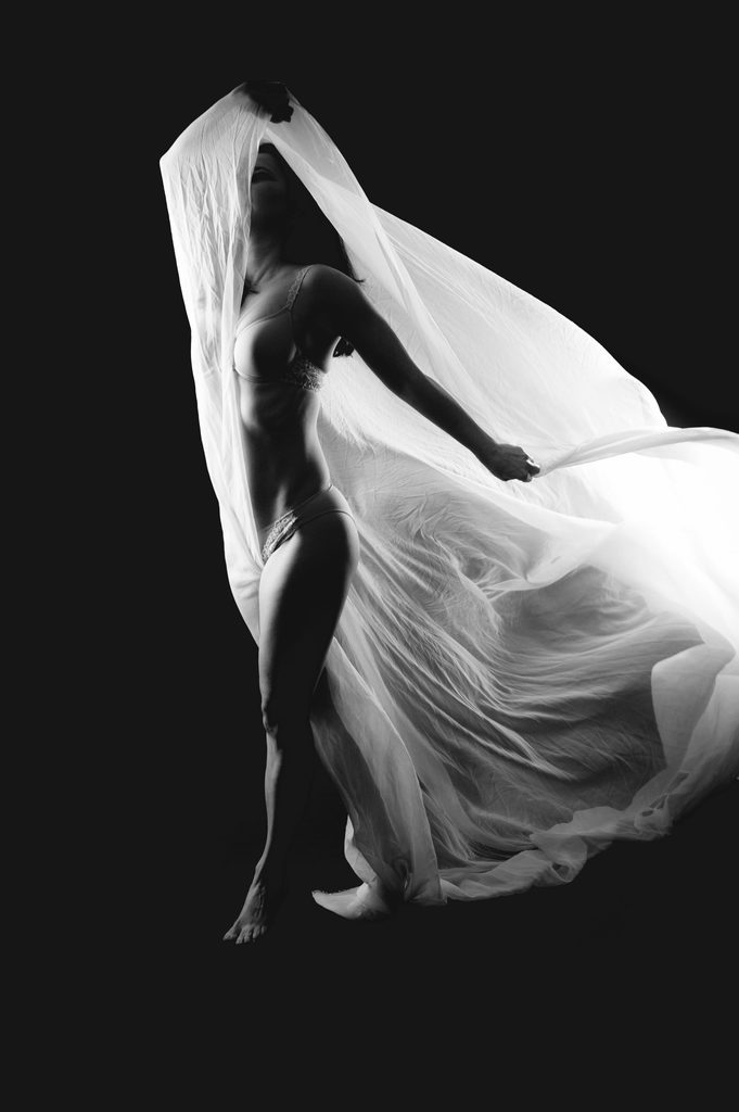 Stilvolle Schwarz-Weiß-Fotografie einer Frau in Dessous mit Tüllstoff vor dunklem Hintergrund, professionelles Fotoshooting im Photogenika Fotostudio in München.