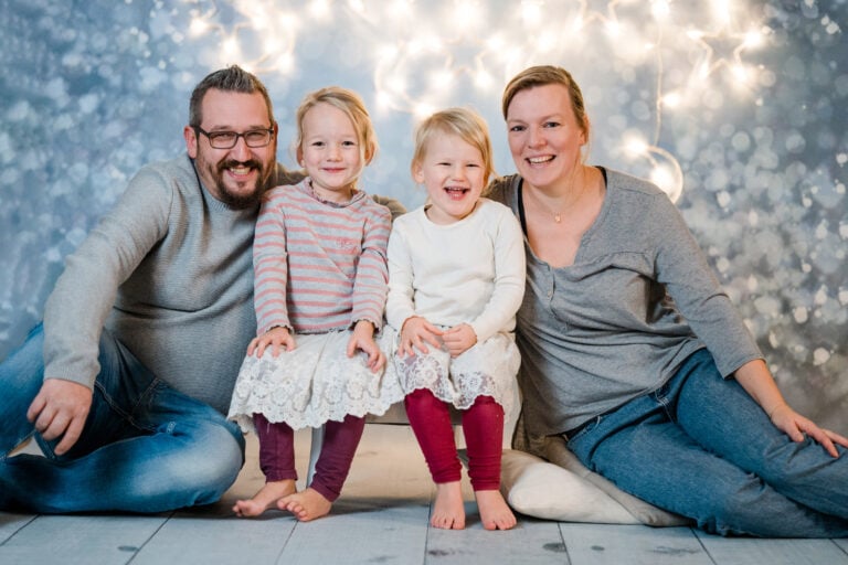 Familienporträt Weihnachten, lachende Eltern mit zwei kleinen Mädchen, festliche Stimmung, Familienfoto, winterliches Ambiente