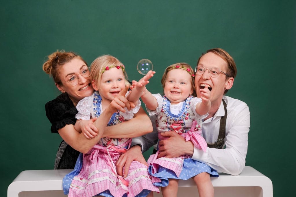 fröhliche familie beim spielen mit seifenblasen, kinder und eltern in traditioneller tracht