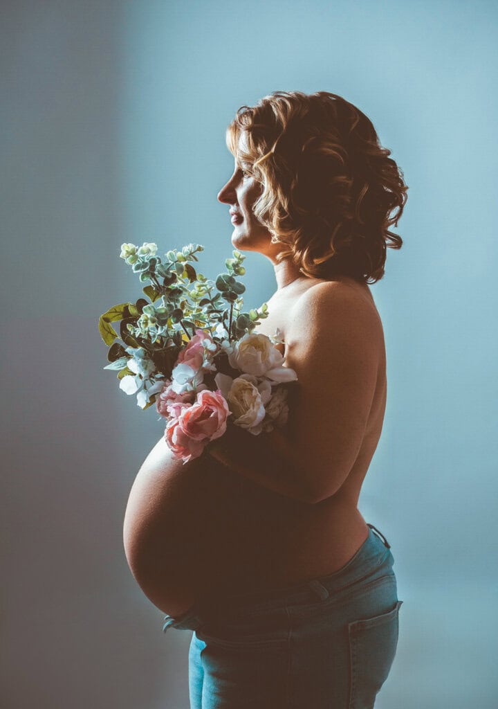 Natürliche Schwangerschaftsfotografie in München, schöne Frau mit Blumen und Babybauch, professionelles Fotoshooting bei Photogenika Fotostudio.