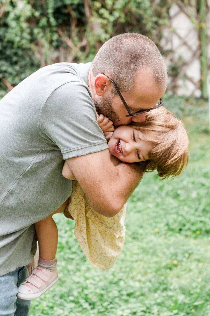 Fröhliches Vater-Kind-Spiel im Garten, lachendes Mädchen mit Papa, Natur, Familie, outdoor, Glücksmoment, authentischer Familienmoment, kreative Fotoshootings, professionelle Kinder- und Familienfotografie in München, Fotostudio Photogenika.