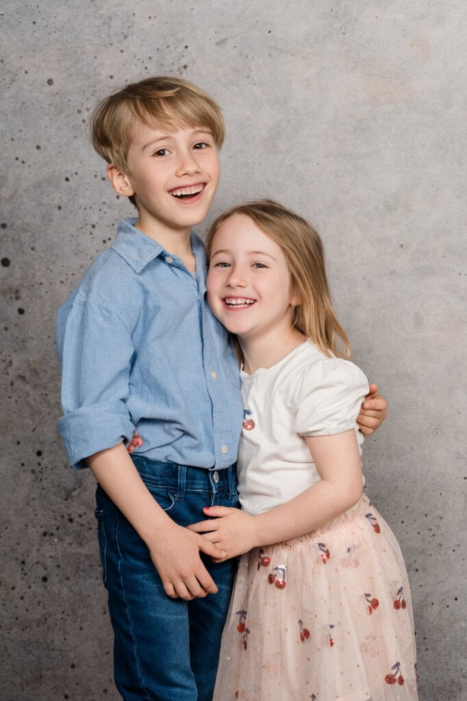 Lachende Geschwister umarmen sich beim Familien-Fotoshooting im Studio.
